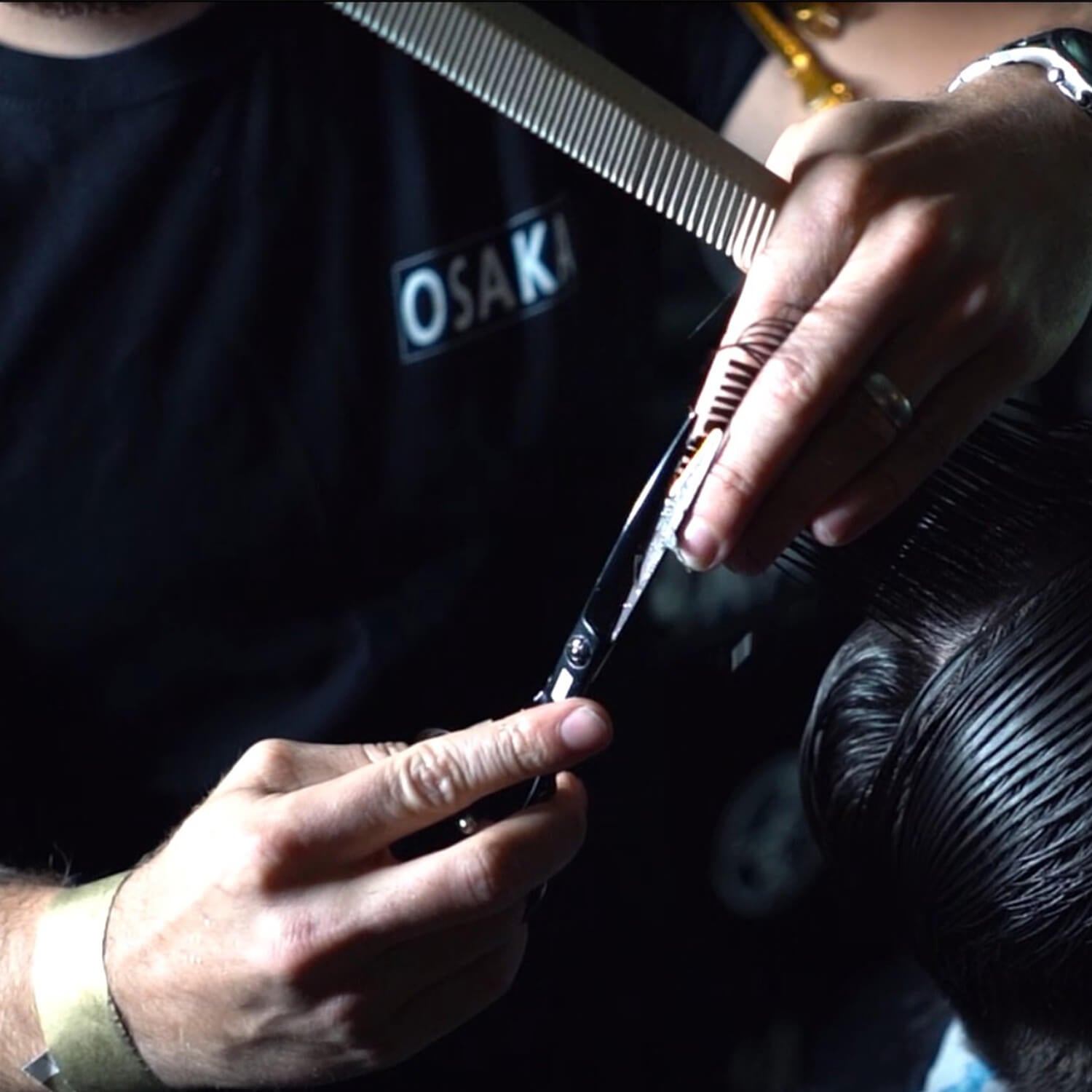 Coiffeur portant le tshirt osaka exécutant une coupe avec les ciseaux osaka noirs